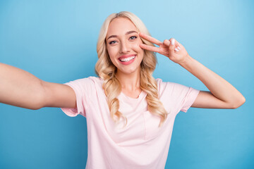 Photo of sweet young blond lady do selfie show v-sign wear pink t-shirt isolated on blue color...