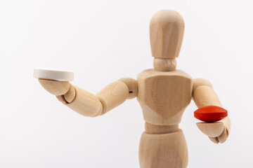 A wooden Gestalta doll or mannequin holds red and white pills in its hands on light background. The concept of choice.