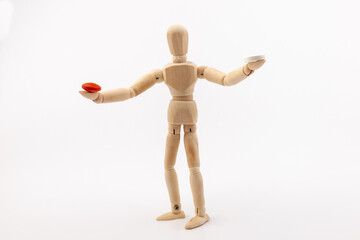 A wooden Gestalta doll or mannequin holds red and white pills in its hands on light background. The concept of choice.