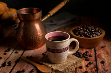 cup of coffee with traditional copper coffee pot with wooden bowl with fresh coffee beans and muffins on wooden table