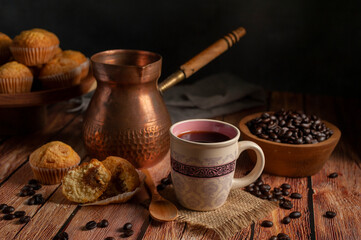 cup of coffee with traditional copper coffee pot with wooden bowl with fresh coffee beans and muffins on wooden table