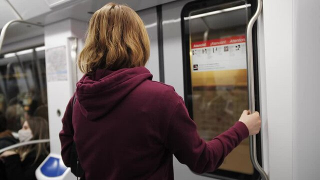 Woman standing in front of the door, get out underground carriage. Student gets off at station.