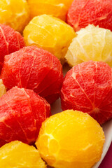 Peeled grapefruits, oroblancos and oranges close-up in an oval dish, top view of citrus fruits on a pink background