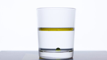 Pour olive oil into a glass of water on a white background