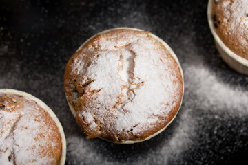 Freshly baked muffins with chocolate and raisins. Spread out on a baking sheet. Some are sprinkled with powdered sugar. Close-up shot.