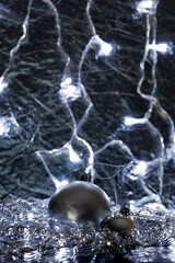 Two silver Christmas tree balls, of different sizes, wrapped in tinsel, on a silver background. Christmas decorations and garlands create a festive atmosphere. Merry Christmas and Happy New Year.