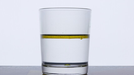 Pour olive oil into a glass of water on a white background