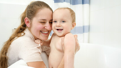 Smiling baby boy washing in bath with foam with mother. Concept of children hygiene, healthcare and development at home