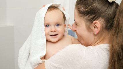 Smiling baby boy hugging mother while she is wiping him and drying with white towel