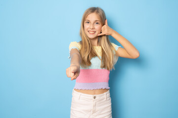 Smiling little girl making call me gesture standing isolated over blue background.