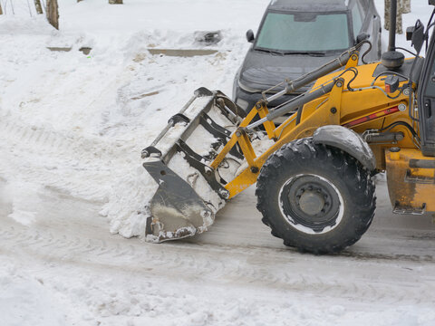 Tractor bulldozer clears snow in the parking lot for cars. Winter works
