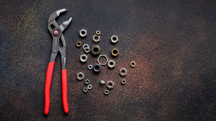 Top view of adjustable universal pliers for repair and assorted nuts on dark rusty background with...