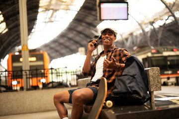 Happy young man waiting for the train. African man waiting in a subway. Man using a phone...