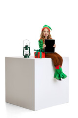 Cute smiling girl dressed like funny gnome or elf using tablet, gadget isolated over white studio background. Winter, holiday, christmas concept