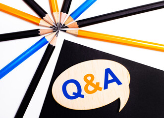 Wooden card with the text QUESTIONS AND ANSWERS on a black background near multicolored pencils.