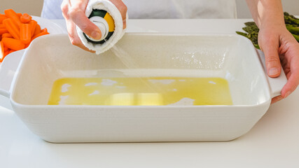 Woman using olive oil spray on a white ceramic baking dish. Cooking process, baked veggies