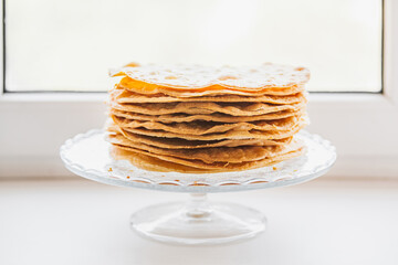 Baked crumpets cakes made of puff pastry for layer cake on a glass stand on windowsill....