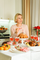 A lovely 40-year-old woman is sitting at a festive table, smiling and holding a candle in her hand. Christmas Holiday, Thanksgiving Day, New Year.