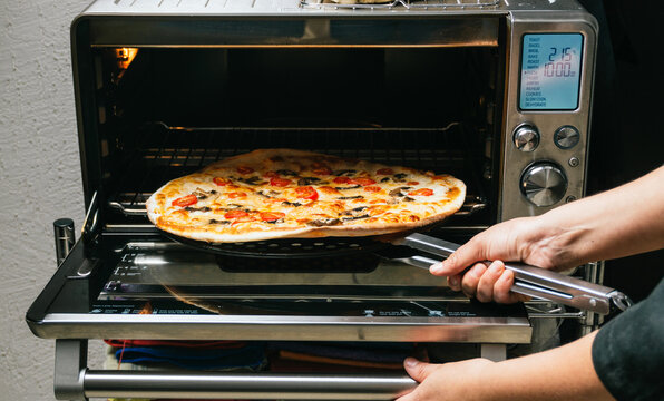 Crop woman taking cooked pizza from oven