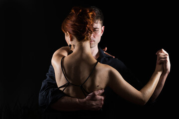 Young couple - a man and a woman wearing black dancing in the dark; the lady stands with her back...