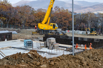 A construction crane in the center of a construction site with an erected foundation.