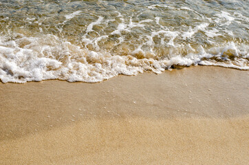 Close-up of a wave crashing onto a sandy shore.