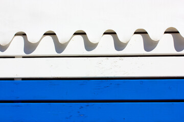 Melting flowing snow on a wooden blue and white fence or wall. Image of snow drifting down. Decorative canopy on a building at a ski resort. Dripping white paint, liquid milk abstract background.