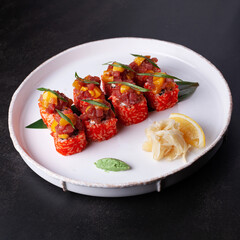 Sushi, red rolls with fish and rice, on a white plate on a dark background, shot from the side