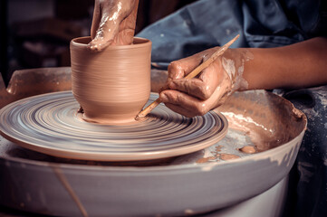 Fototapeta na wymiar Master-ceramist creates a clay pot on a potter's wheel. Hands of potter close up. Ancient craft and pottery handmade work