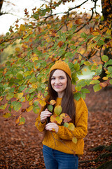 Smiling white young european woman in yellow sweater near the trees in autumn park