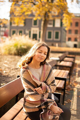 White young european woman with brown hair with closed eyes sitting on bench in sunny autumn