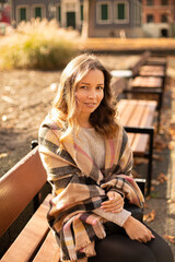 Fototapeta premium European white young woman with brown hair sitting on bench in sunny autumn