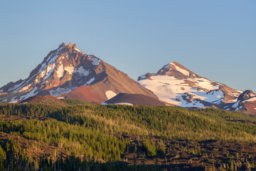 USA, Oregon. Three Sisters Wilderness, North (left) and Middle Sister (right) rise above conifers...