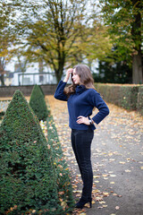 Young european woman in dark blue jumper with long curly hair in autumn park holding hand near forehead