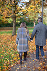 Obraz premium Turned back white young man and woman in autumn forest holding hands