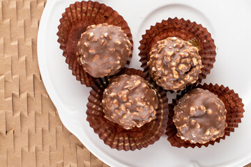 Several sweet chocolates with nuts with white dishes on craft paper, close-up, top view.