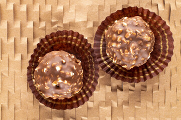 Two sweet chocolate candies with nuts on craft paper, close-up, top view.