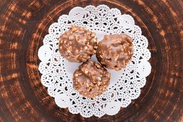 Three sweet chocolates with nuts on a clay platter, close-up, top view.