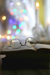 Fototapeta na wymiar Open book and reading glasses with candles and colorful bokeh lights in the background. Selective focus.