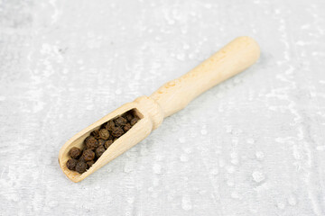 Lot of whole spicy black pepper in a wooden scoop on white background