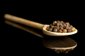 Lot of whole spicy black pepper in a wooden spoon isolated on black glass