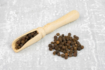 Lot of whole spicy black pepper in a wooden scoop on white background with small group pepper aside