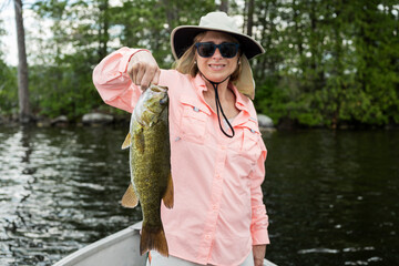 Woman fishing on a lake holding big bass catch. Lady holding large smallmouth bass catch. - obrazy, fototapety, plakaty