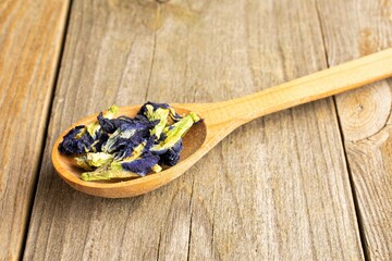 Lot of whole dry clitoria ternatea in a wooden spoon on old wood in closeup