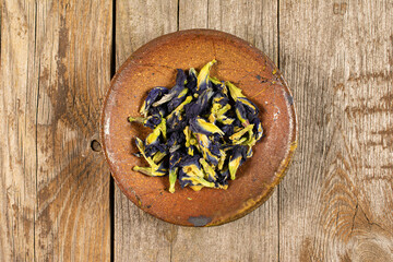 Lot of whole dry clitoria ternatea in ceramic bowl on old wood flatlay