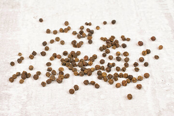 Lot of whole spicy black pepper on white background