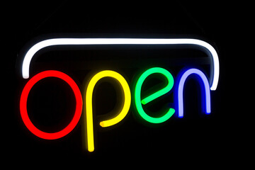 A neon sign that reads "Open" hangs on a black background. Neon Light "Open" Sign hanging above building at night. Glowing open neon sign in a window.
