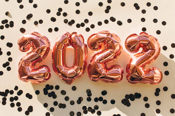 Balloons made of pink foil in the form of numbers 2022 with black confetti on a pink background. Celebrating Christmas, New Year and festive concept. Flat lay, top view.