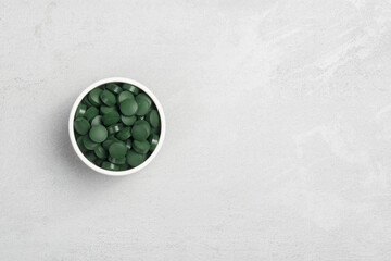 Obraz na płótnie Canvas A bowl with spirulina tablets on a gray background, a place for text