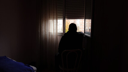 a man sits in a dark room and looks out of an open window